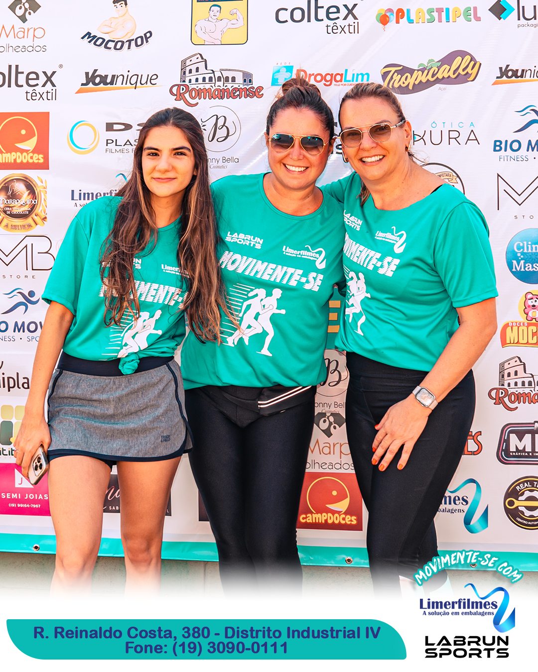 Três participantes do treinão beneficente diante do painel de patrocinadores